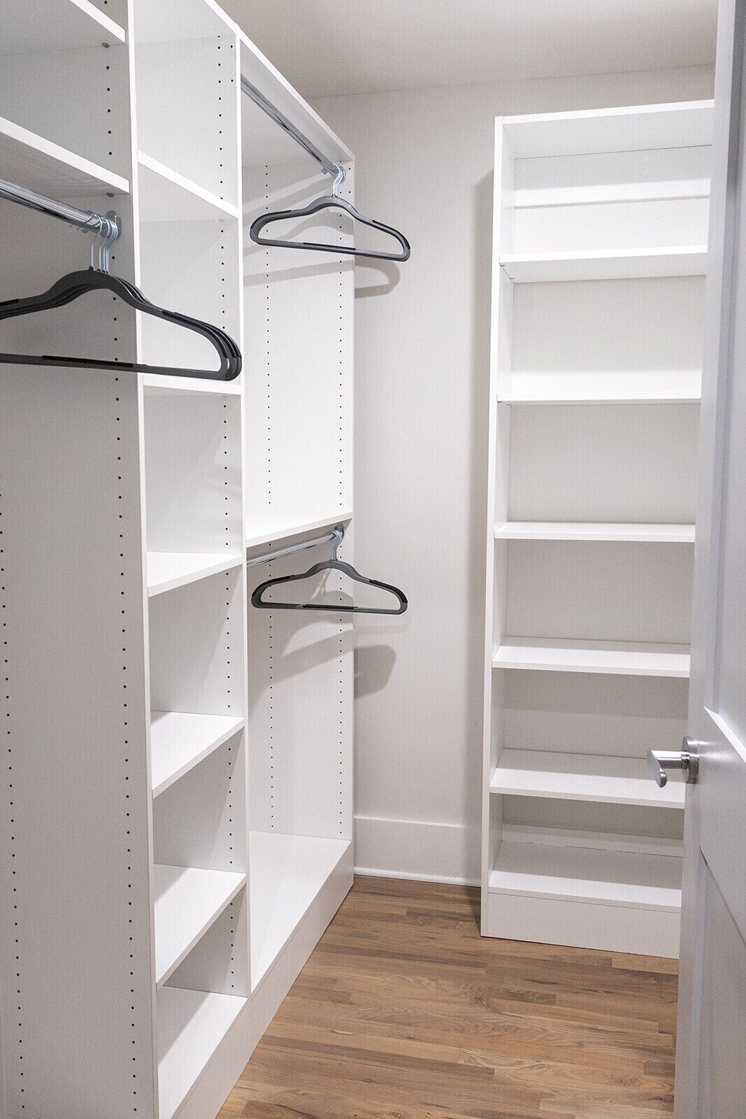 A walk-in closet with white shelving units and metal hangers.