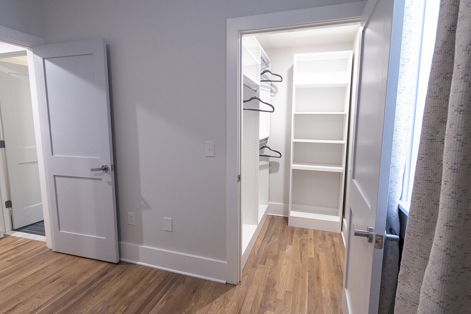 A hallway leading to a closet with shelves and hanging space.