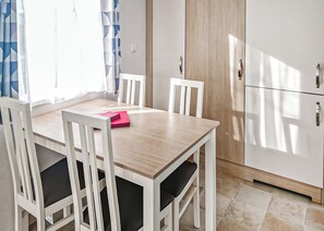 Un coin repas avec une table en bois et des chaises blanches, un meuble blanc et une fenêtre ornée de rideaux bleus.