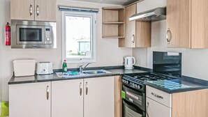 A compact kitchenette with a microwave, toaster, sink, stove, and oven. - York Standard Caravan (Thirsk)