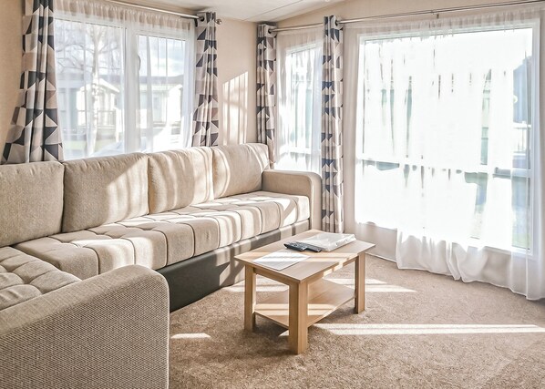 A living room with a sofa, a coffee table, and large windows with curtains.