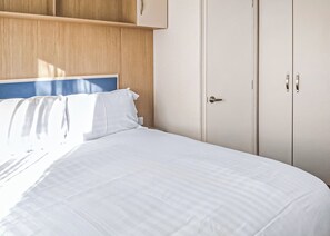 Una cama con ropa de cama blanca, un cabecero de madera y un armario con una puerta.