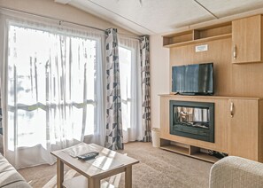 A living room with a television on a wooden cabinet, a fireplace, and a table with a remote control. - York Standard Caravan (Thirsk)