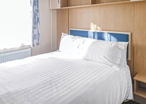 Un lit bien fait, avec une literie blanche, une tête de lit en bois et une fenêtre ornée de rideaux bleus.