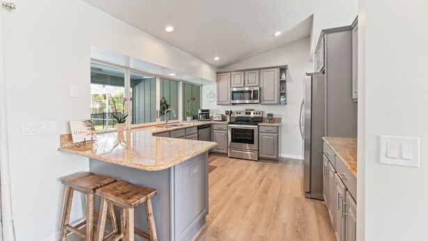 A modern kitchen with a central island, stainless steel appliances, and wooden flooring. - Completely renovated! Private 3/2/2 heated pool home in Port St Lucie FL! (Port St. Lucie)