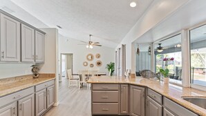 A spacious kitchen with granite countertops, a central island, and a dining area with white chairs. - Completely renovated! Private 3/2/2 heated pool home in Port St Lucie FL! (Port St. Lucie)