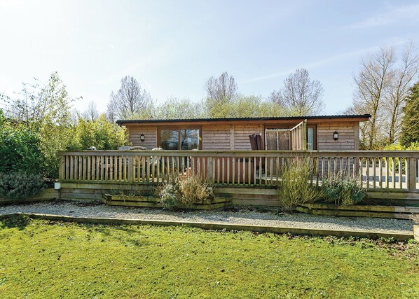 A wooden cabin with a deck, surrounded by greenery and trees.