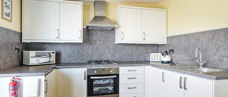 A kitchen with white cabinets, a gas stove, an oven, a microwave, and a sink.