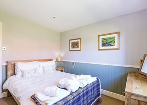A bedroom with a bed, two framed artworks, a bedside lamp, and a wooden nightstand.