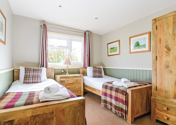 A bedroom with two beds, a wooden wardrobe, a window with curtains, and two framed pictures on the wall.