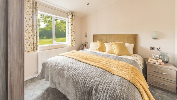Un dormitorio con cama, mesita de noche, lámpara y ventana con cortinas.