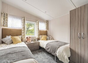 A bedroom with two beds, a wardrobe, a window with curtains, and a teddy bear on the nightstand. - 3 bedroom accommodation in Glenluce, Newton Stewart (Glenluce, Newton Stewart)