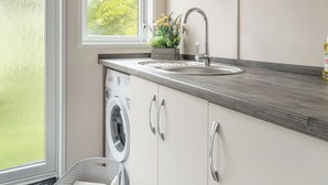 Una cocina moderna con lavadora integrada, un lavamanos y una ventana con vistas a zonas verdes.