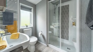 Un baño moderno con ducha envuelta en vidrio, un lavamanos blanco, un inodoro y una ventana con persianas.