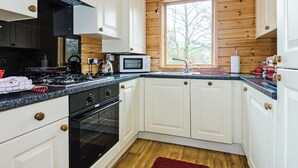 Une cuisine avec des meubles blancs, une cuisinière noire, un four à micro-ondes et une fenêtre donnant sur des arbres.