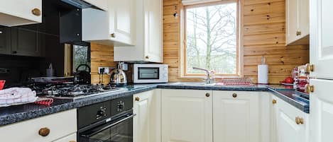 A kitchen with white cabinets, a black stove, a microwave, and a window with a view of trees.