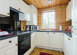 A kitchen with white cabinets, a black stove, a microwave, and a window with a view of trees.