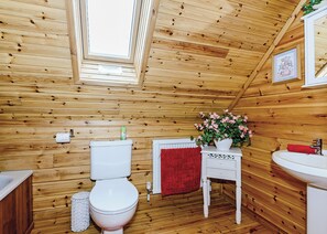 A wooden cabin bathroom with a toilet, sink, and a red towel.