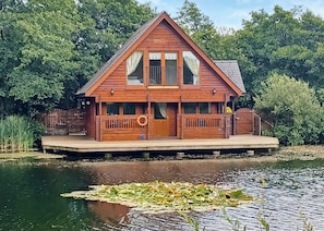 A wooden cabin with a balcony, a dock, and a pond with lily pads. - Set in a peaceful location and perched over the lake. (Anglesey)