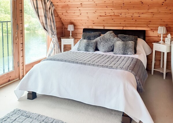 A bedroom with a bed, pillows, a nightstand, a lamp, and a view of the outdoors.