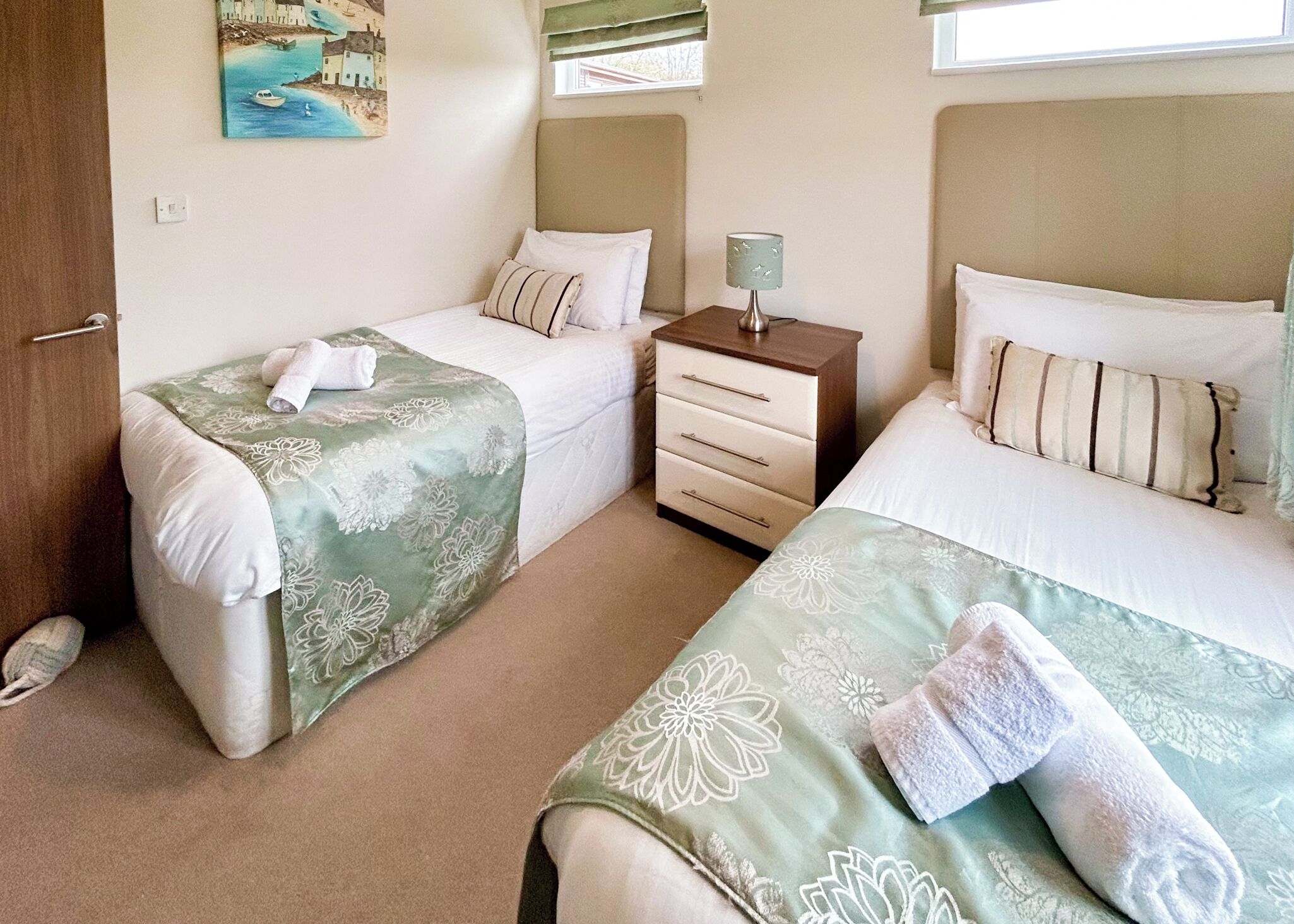 A bedroom with two beds, a nightstand, a lamp, and a painting on the wall.