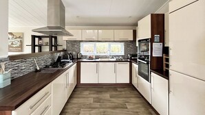 A modern kitchen with a central island, stainless steel appliances, and a window providing natural light. - Country Lodge Four Platinum (Tintagel)