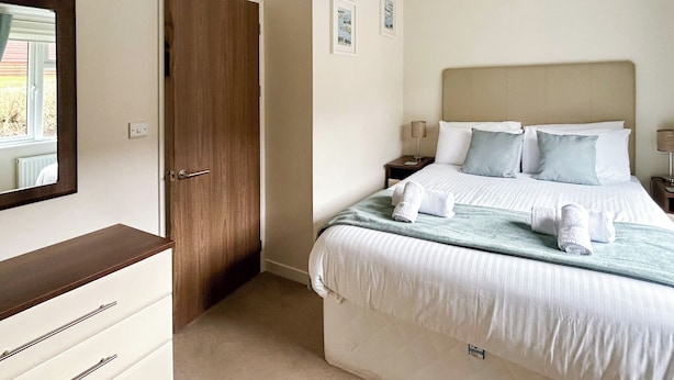 A hotel room with a bed, a dresser, a door, and a mirror. - Country Lodge Four Platinum (Tintagel)
