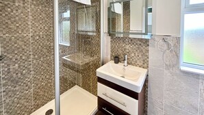 A bathroom with a glass shower enclosure, a sink with a mirror above it, and a window to the right. - Country Lodge Four Platinum (Tintagel)