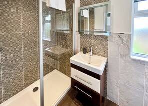 Un baño con cabina de ducha de vidrio, un lavabo con espejo y una ventana a la derecha.