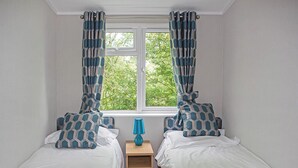 Une chambre avec deux lits, une fenêtre et une table de chevet avec une lampe.