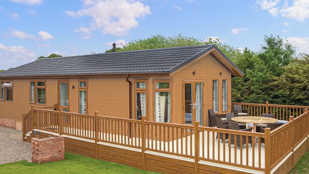 Une cabane en bois avec une terrasse, un patio doté d’une table et de chaises, et une cheminée en briques.