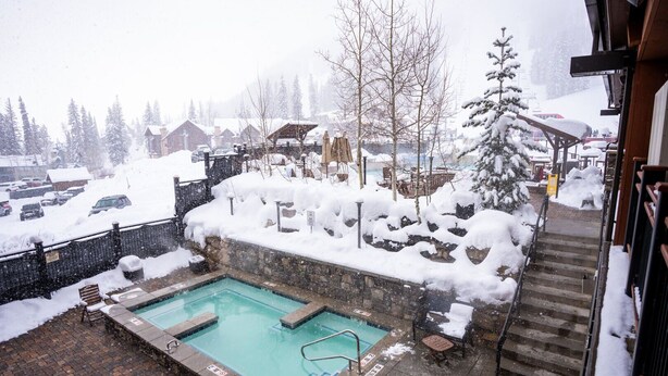 A pool area with a stone wall, a wooden deck, and a view of a snowy village in the background. - All the comforts of home. Amazing mountain views from both floors! (Durango)