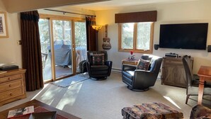 A spacious living room with a sliding glass door leading to a balcony, a flat-screen TV mounted on the wall, and a wooden dining table. - All the comforts of home. Amazing mountain views from both floors! (Durango)