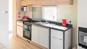 A compact kitchen with a stove, oven, sink, and a microwave. - Caravan with one double and one twin. (Cargill)