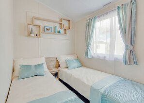 Ein Schlafzimmer mit zwei Betten, einem Fenster mit durchsichtigen Vorhängen und einem Regal mit Dekoration.