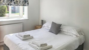 Een net opgemaakt bed met witte lakens en opgevouwen handdoeken, een nachtkastje met een lamp, en een raam met uitzicht op het omliggende landschap.