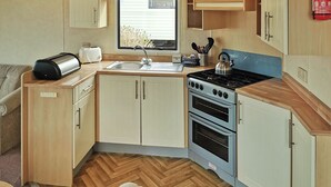 A compact kitchen with a sink, stove, and oven, wooden cabinets, and a window. - 2 bedroom accommodation in Clarach Bay, Nr Aberystwyth (Clarach Bay, Nr Aberystwyth)