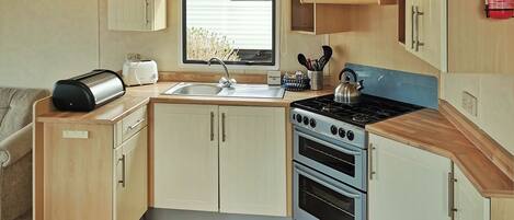 A compact kitchen with a sink, stove, and oven, wooden cabinets, and a window.
