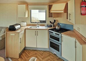 A compact kitchen with a sink, stove, and oven, wooden cabinets, and a window.