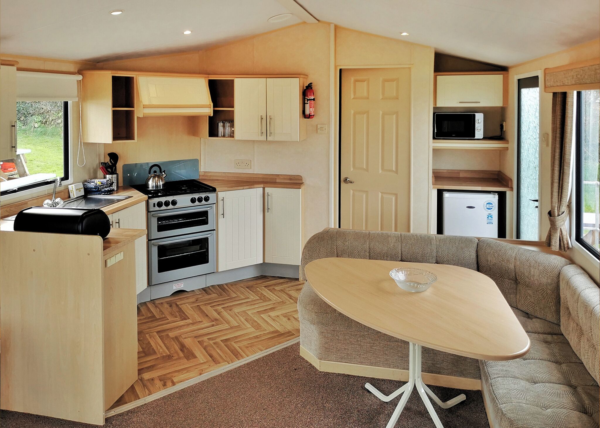 A compact kitchen with a stove, oven, and microwave, a dining area with a table and sofa, and a door leading to a small living space.
