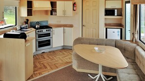 Une cuisine compacte équipée d’une cuisinière, d’un four et d’un micro-ondes, un coin repas avec une table et un canapé, et une porte donnant sur un petit espace de vie.