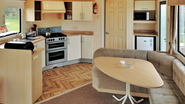 A compact kitchen with a stove, oven, and microwave, a dining area with a table and sofa, and a door leading to a small living space. - 2 bedroom accommodation in Clarach Bay, Nr Aberystwyth (Clarach Bay, Nr Aberystwyth)