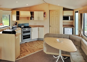 A compact kitchen with a stove, oven, and microwave, a dining area with a table and sofa, and a door leading to a small living space.