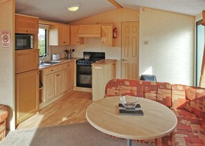 A compact RV kitchen with wooden cabinets, a microwave, stove, and a small table with a bowl.