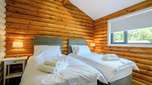 Une chambre située dans un chalet en rondins, avec deux lits, une fenêtre et une table de chevet avec une lampe.