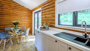 L’intérieur d’une cabane en rondins comprend un coin repas, une cuisine et de grandes fenêtres.