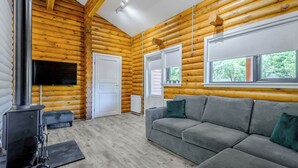 L’intérieur d’une cabane en rondins, avec un canapé, une cheminée et de grandes fenêtres.