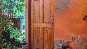 A wooden door with a sign reading "CORCOVADO," a bench with a quilted cushion, and potted plants in a courtyard. -  Gardens House, Airport Juan Santamaría, Alajuela, San Jose (Alajuela)