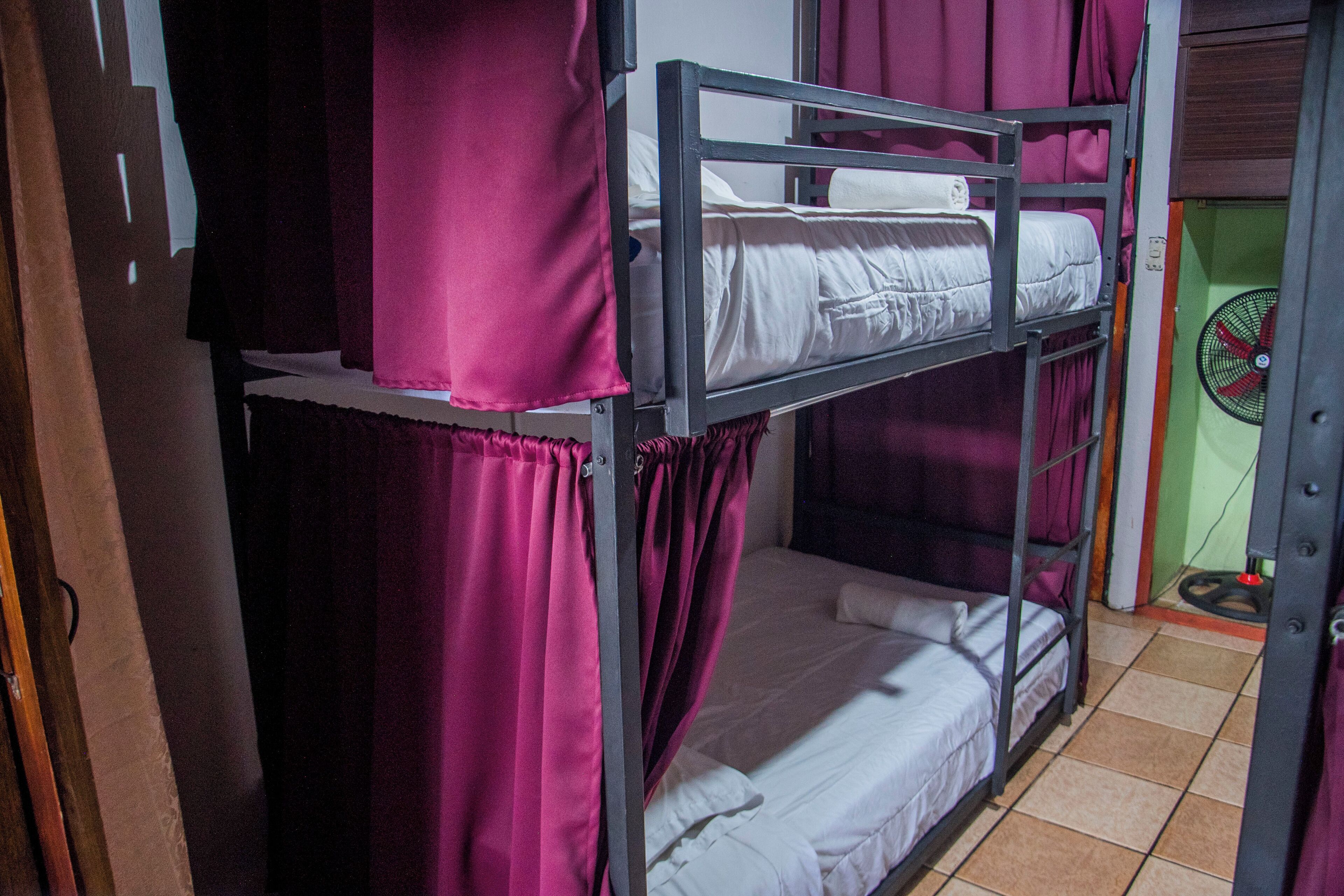 Habitación con literas, cortinas y un ventilador.
