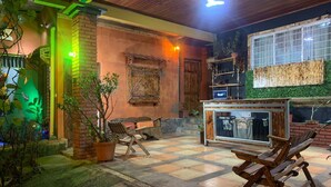 An outdoor seating area with wooden furniture, a brick wall, and a window with a view of the sky. -  Gardens House, Airport Juan Santamaría, Alajuela, San Jose (Alajuela)